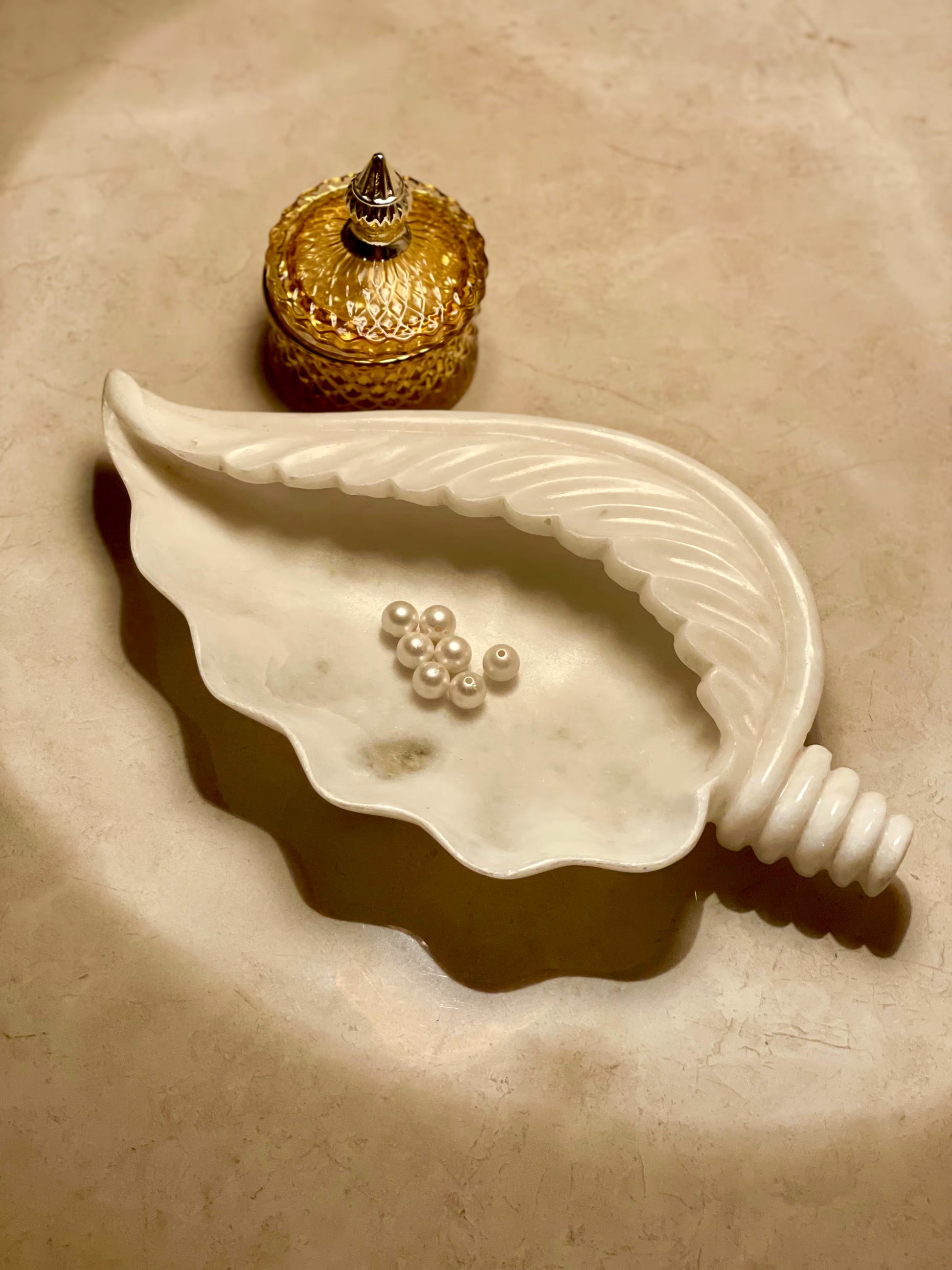 Decorative shell with pearls and a small decorative bottle on a beige surface